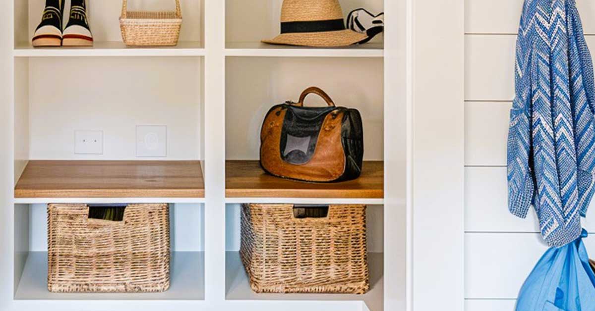 An organized shelf with woven baskets, shoes, a straw hat, a leather bag, and a blue patterned garment hanging, showcasing a balance between practicality and idealism in decluttering.