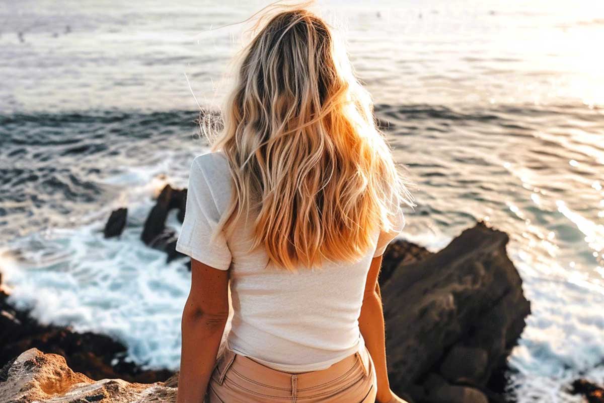 A woman with blonde hair overlooks a rocky coastline at sunset, reflecting the calm of a minimalist mindset.