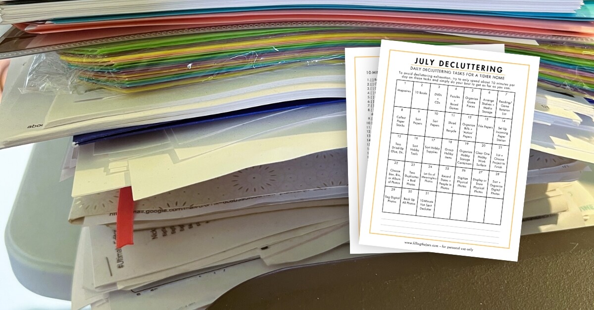 A printed July declutter calendar showing daily decluttering tasks designed to help organize and tidy a home, placed over a large stack of papers and documents.