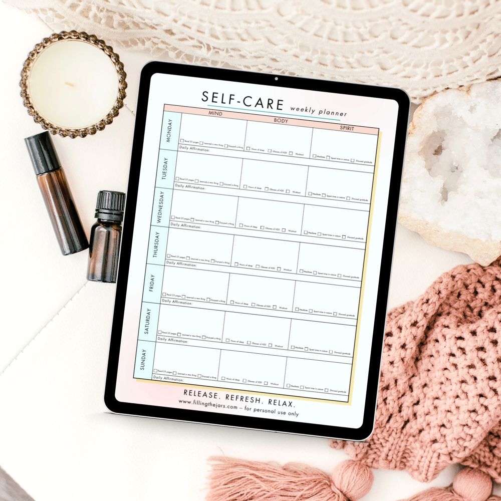 Tablet showing a self care weekly planner beside a candle. essential oil bottle. makeup tube. crystal. and pink knit blanket. Text reads "SELF CARE weekly planner".